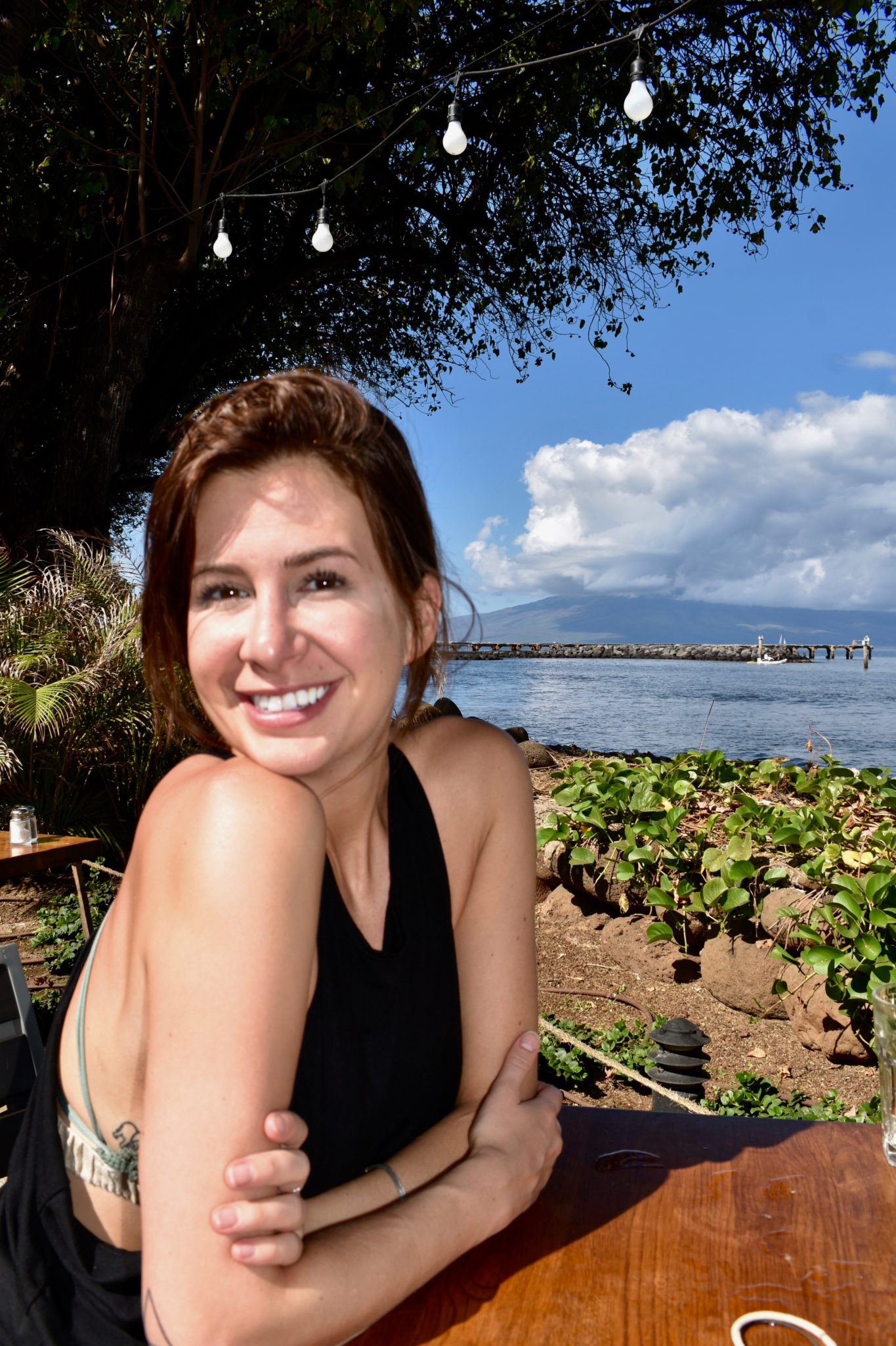 Carmen with a huge smile on her face, sitting at the table in front of the ocean